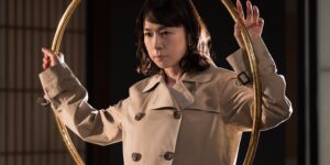 NHKのコント番組LIFE!にて女神探偵・輪島ナオミを演じる西田尚美さん。金色のフープを背面に構えている。